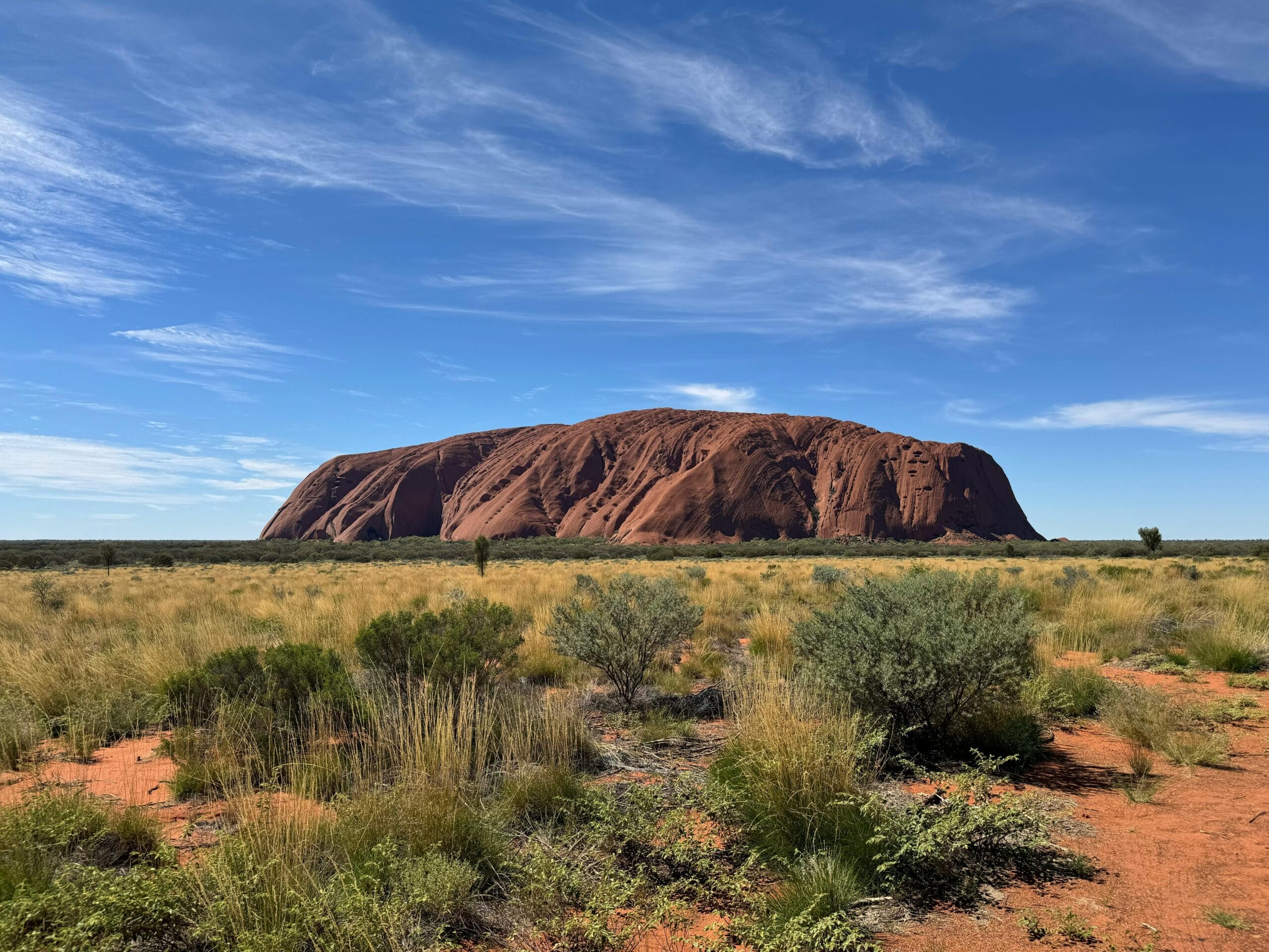 Breathtaking view of Uluru surrounded by Australian desert landscape under a bright blue sky.