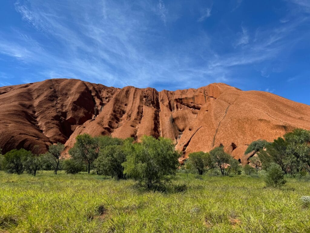 Stunning view of Uluru's red rock under a clear blue sky with lush greenery.