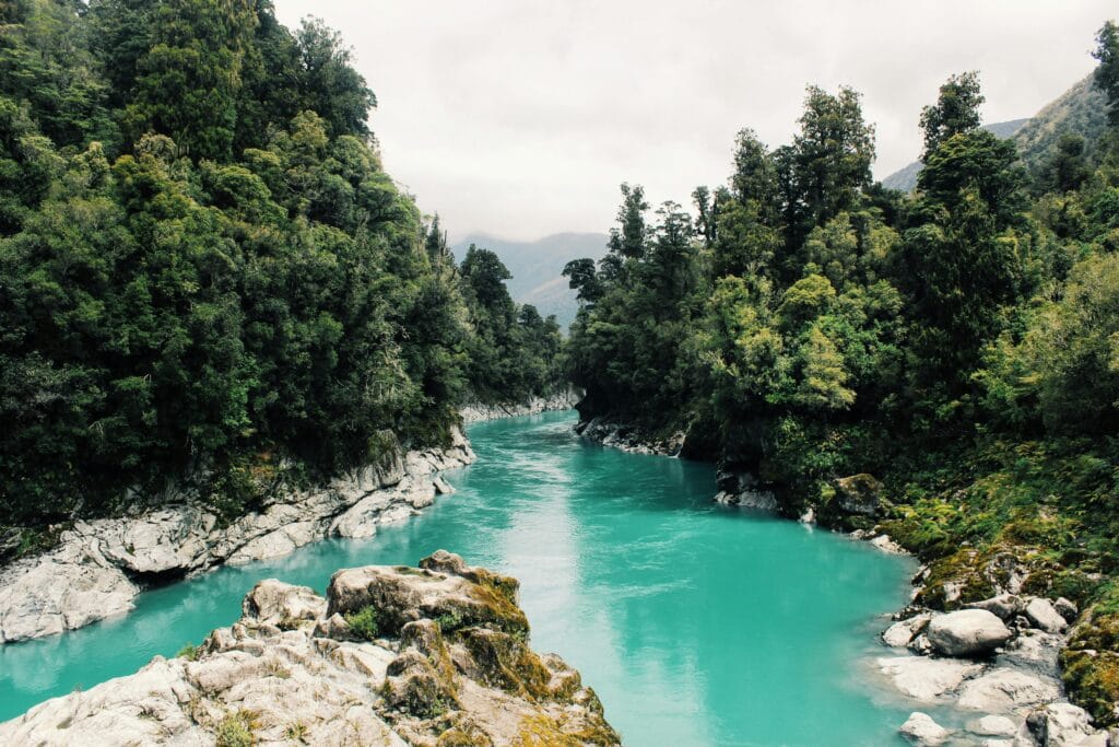 Beautiful turquoise river winding through a dense, lush forest under a cloudy sky.