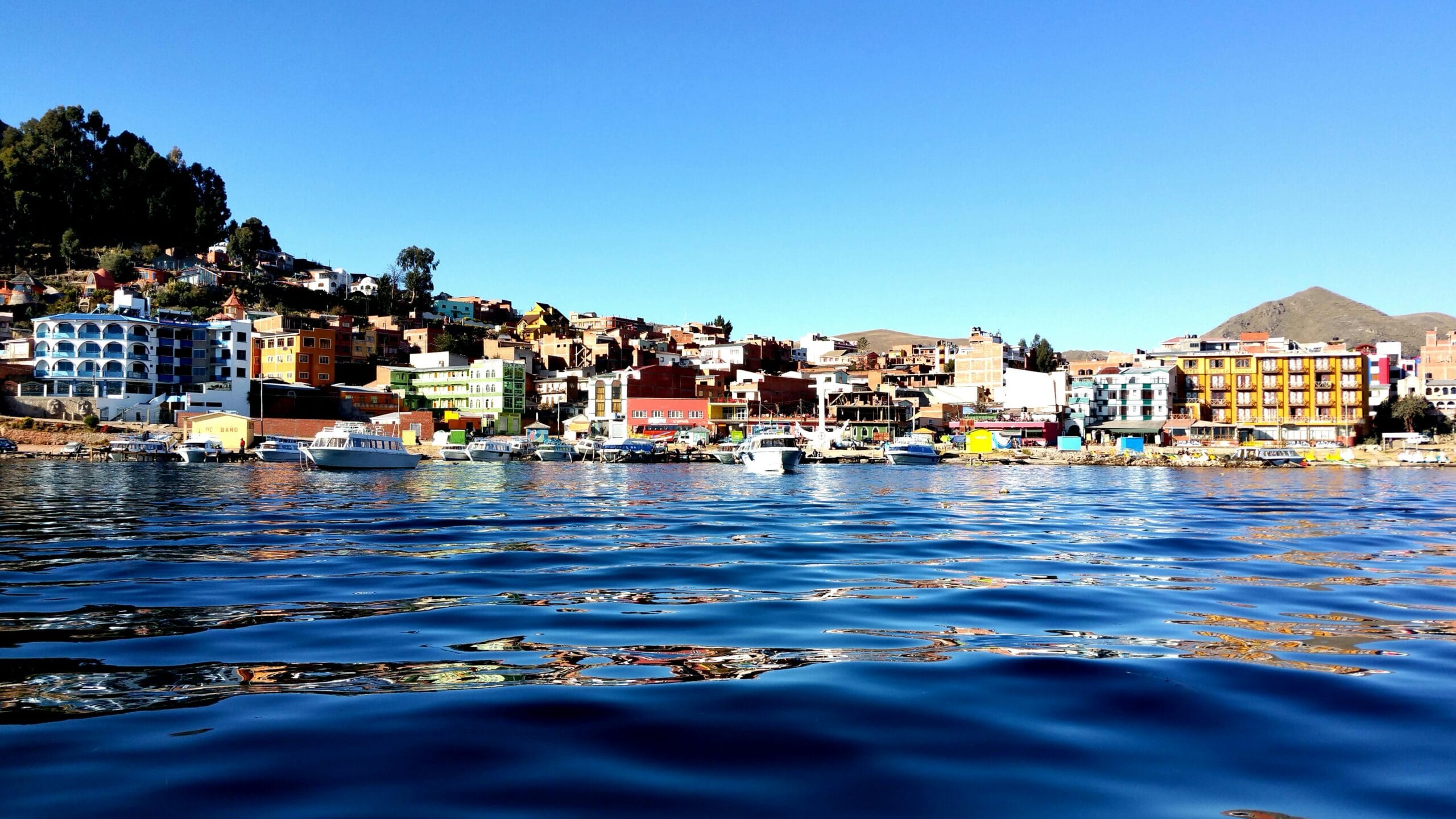 Vibrant shoreline view of Copacabana town with boats on Lake Titicaca under clear blue sky.